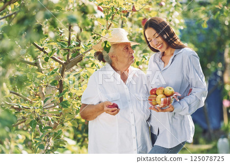 Holding fresh apples. Young woman is with her senior mother is in the garden 125078725