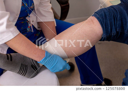 A medical professional is bandaging a patients injured leg for proper healing and protection A medical professional is bandaging a patients injured leg for proper healing and protection 125078800