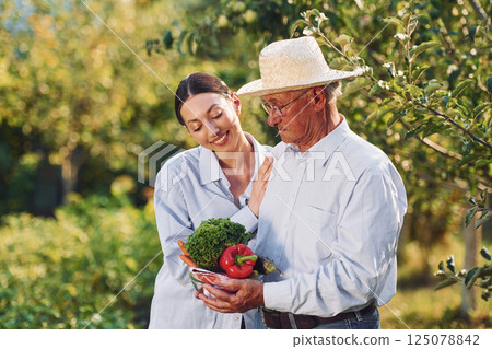 With vegetables in hands. Daughter is with her senior father in the garden at daytime 125078842