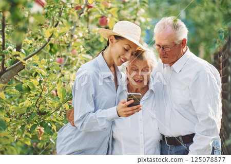 Woman showing something on the smartphone. Daughter is with her senior mother and father is in the garden 125078877