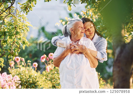 Standing in the beautiful garden and embracing each other. Young woman is with her senior mother 125078958