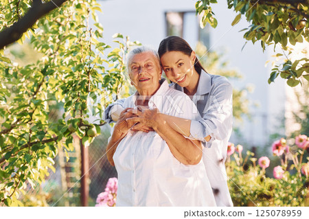 Standing in the beautiful garden and embracing each other. Young woman is with her senior mother Standing in the beautiful garden and embracing each other. Young woman is with her senior mother 125078959