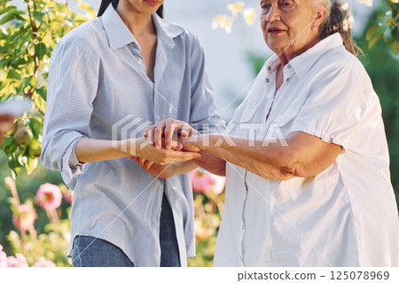 Holding each other's hands. Young woman is with her senior mother is in the garden 125078969