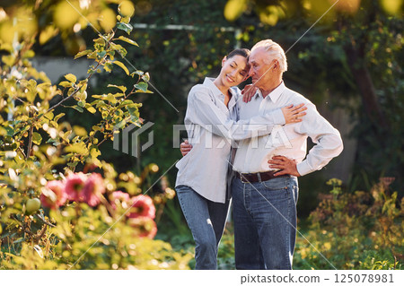 Standing and posing. Daughter is with her senior father in the garden at daytime Standing and posing. Daughter is with her senior father in the garden at daytime 125078981
