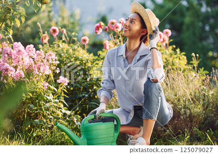 Preparing for watering the flowers. Young cheerful woman is in the garden at daytime Preparing for watering the flowers. Young cheerful woman is in the garden at daytime 125079027