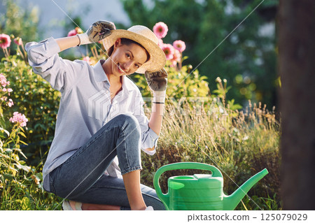 Preparing for watering the flowers. Young cheerful woman is in the garden at daytime 125079029
