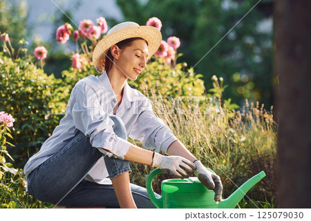 Sitting on the ground. Young cheerful woman is in the garden at daytime Sitting on the ground. Young cheerful woman is in the garden at daytime 125079030