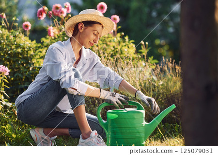 With green water can. Young cheerful woman is in the garden at daytime 125079031