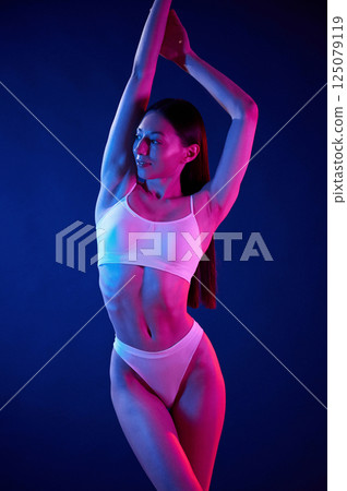 Standing with hands up. Young woman in underwear is in the studio with neon lights Standing with hands up. Young woman in underwear is in the studio with neon lights 125079119