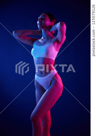 Showing body. Young woman in underwear is in the studio with neon lights Showing body. Young woman in underwear is in the studio with neon lights 125079126