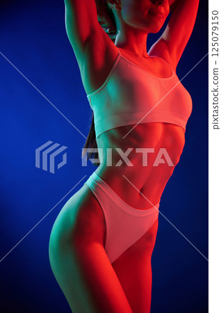 Illuminated by red color. Young woman in underwear is in the studio with neon lights 125079150