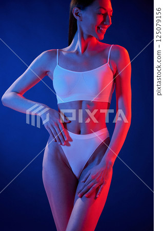 Slim body type. Young woman in underwear is in the studio with neon lights Slim body type. Young woman in underwear is in the studio with neon lights 125079156