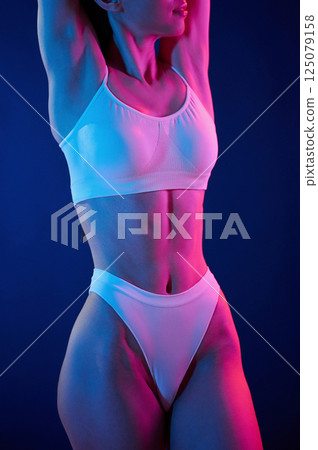 Slim body type. Young woman in underwear is in the studio with neon lights Slim body type. Young woman in underwear is in the studio with neon lights 125079158