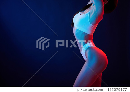 Beautiful slim body type. Young woman in underwear is in the studio with neon lights Beautiful slim body type. Young woman in underwear is in the studio with neon lights 125079177
