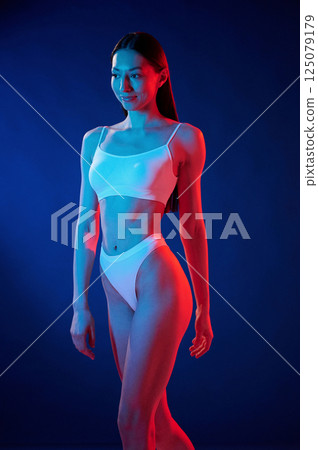 Beautiful slim body type. Young woman in underwear is in the studio with neon lights 125079179