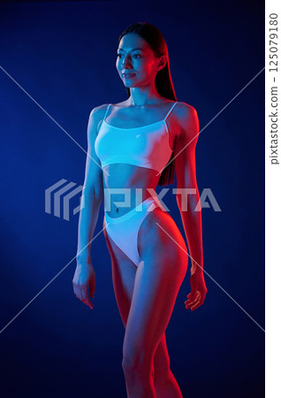 Beautiful slim body type. Young woman in underwear is in the studio with neon lights 125079180