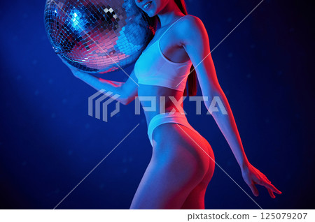 With shiny mirrored ball. Young woman in underwear is in the studio with neon lights 125079207