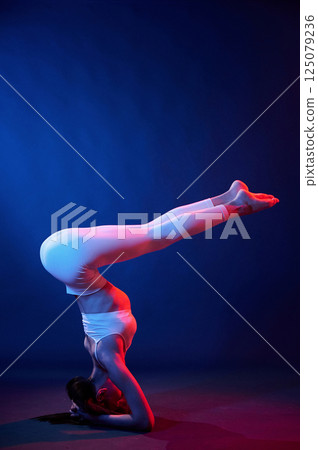 Doing head stand. Young woman in sportive clothes is in the studio with neon lights Doing head stand. Young woman in sportive clothes is in the studio with neon lights 125079236