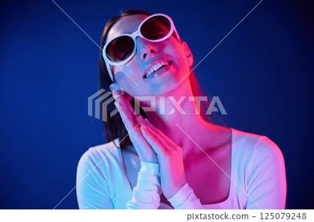 In sunglasses. Portrait of young woman that is indoors in neon lighting In sunglasses. Portrait of young woman that is indoors in neon lighting 125079248