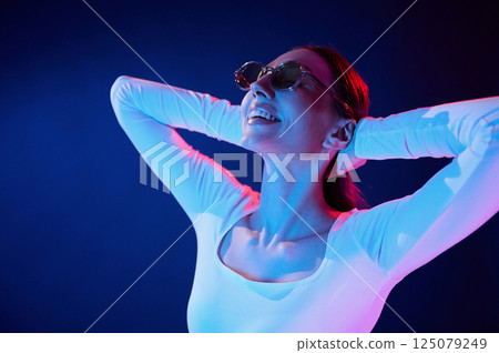 In sunglasses. Portrait of young woman that is indoors in neon lighting 125079249