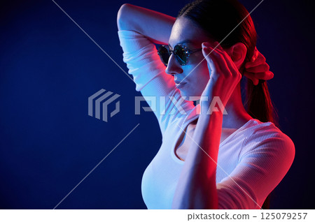 Standing and posing. Portrait of young woman that is indoors in neon lighting Standing and posing. Portrait of young woman that is indoors in neon lighting 125079257