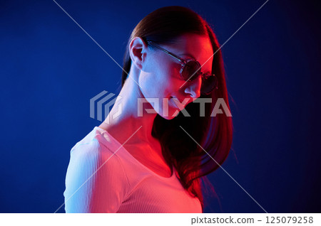 Standing and posing. Portrait of young woman that is indoors in neon lighting Standing and posing. Portrait of young woman that is indoors in neon lighting 125079258