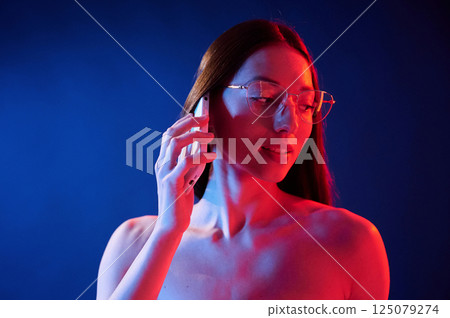 Talking by the phone. Portrait of young woman that is indoors in neon lighting 125079274