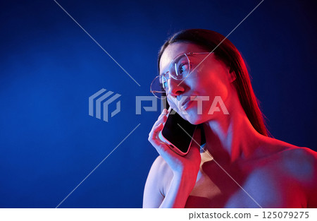 Talking by the phone. Portrait of young woman that is indoors in neon lighting Talking by the phone. Portrait of young woman that is indoors in neon lighting 125079275