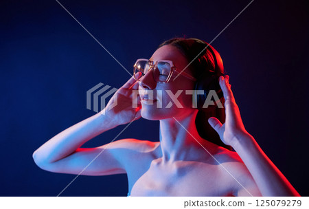 Enjoying music by using headphones. Portrait of young woman that is indoors in neon lighting 125079279