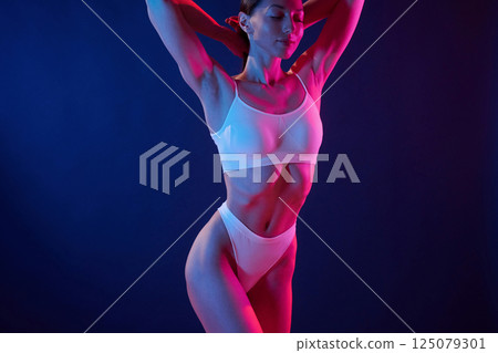 Fitness type body. Young woman in underwear is in the studio with neon lights Fitness type body. Young woman in underwear is in the studio with neon lights 125079301