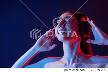 Feel the music. In headphones. Portrait of young woman that is indoors in neon lighting 125079344