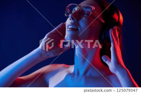 Feel the music. In headphones. Portrait of young woman that is indoors in neon lighting Feel the music. In headphones. Portrait of young woman that is indoors in neon lighting 125079347