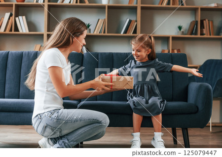 Happy little girl is with gift box. Young mother with her daughter is together at apartment Happy little girl is with gift box. Young mother with her daughter is together at apartment 125079447