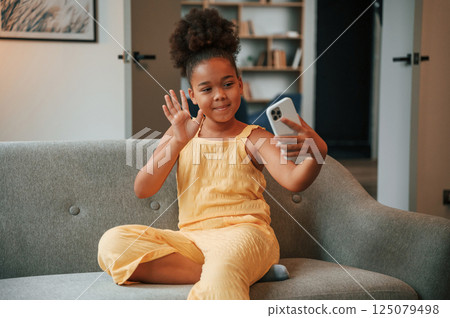 Making a selfie. Cute black girl in casual clothes is at home at daytime Making a selfie. Cute black girl in casual clothes is at home at daytime 125079498