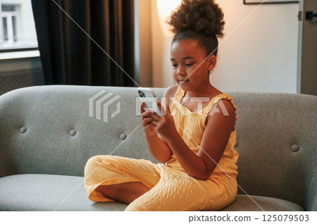 Surfing the internet by using smartphone. Cute black girl in casual clothes is at home at daytime 125079503