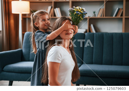 Girl is giving beautiful flowers to a woman. Young mother with her daughter is together at apartment Girl is giving beautiful flowers to a woman. Young mother with her daughter is together at apartment 125079603