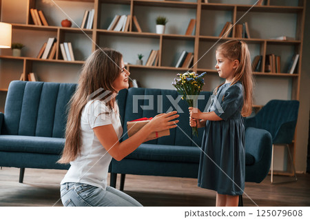Girl is giving beautiful flowers to a woman. Young mother with her daughter is together at apartment 125079608