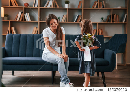 Conception of mother's day. Giving gift. Young woman with her daughter is together at apartment 125079620
