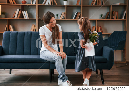 Conception of mother's day. Giving gift. Young woman with her daughter is together at apartment 125079621