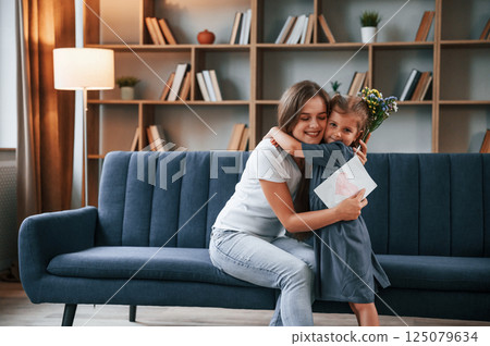 Embracing each other. Giving the gift. Young mother with her daughter is together at apartment Embracing each other. Giving the gift. Young mother with her daughter is together at apartment 125079634