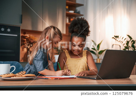 Two little girls sitting by the table and drawing 125079676