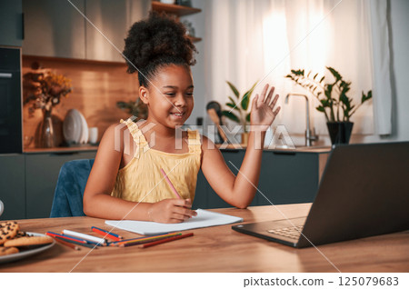 Having online study. Cute black girl in casual clothes is at home at daytime Having online study. Cute black girl in casual clothes is at home at daytime 125079683