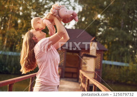 Holding baby in hands. Mother with her newborn son is outdoors on the lawn at the daytime 125079732