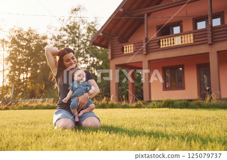 Mother with her newborn son is outdoors on the lawn at the daytime 125079737
