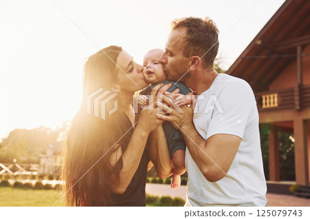 Kissing the baby. Happy parents with their son newborn outdoors having a weekend 125079743