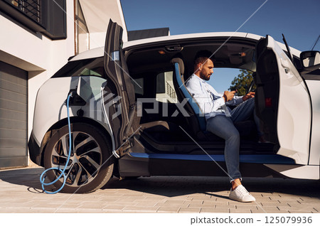 Sitting in the vehicle. Young stylish man is with electric car at daytime 125079936