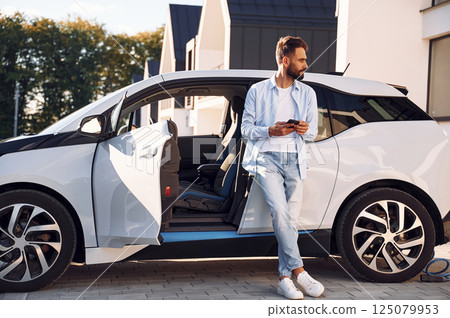 Young stylish man is with electric car at daytime Young stylish man is with electric car at daytime 125079953