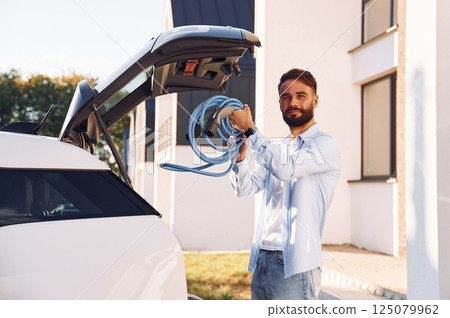 Taking charging wire from the truck. Young stylish man is with electric car at daytime 125079962