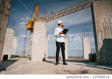 Inspector with notepad is standing on the construction site Inspector with notepad is standing on the construction site 125080019