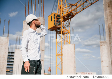 Inspector with notepad is standing on the construction site Inspector with notepad is standing on the construction site 125080020
